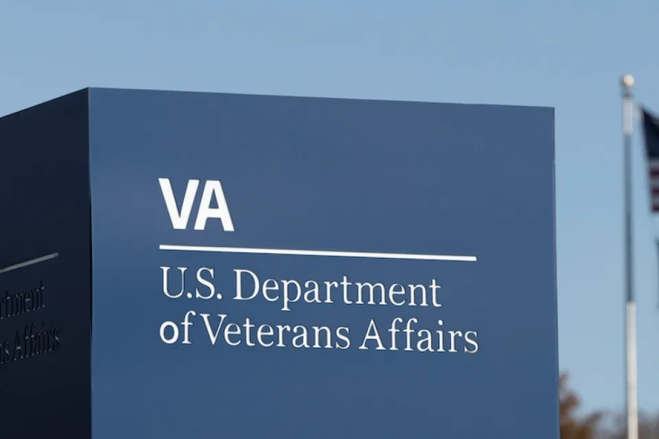 Close-up of Department of Veterans Affairs sign in Washington, D.C. with American and MIA flags on flagpole in background.